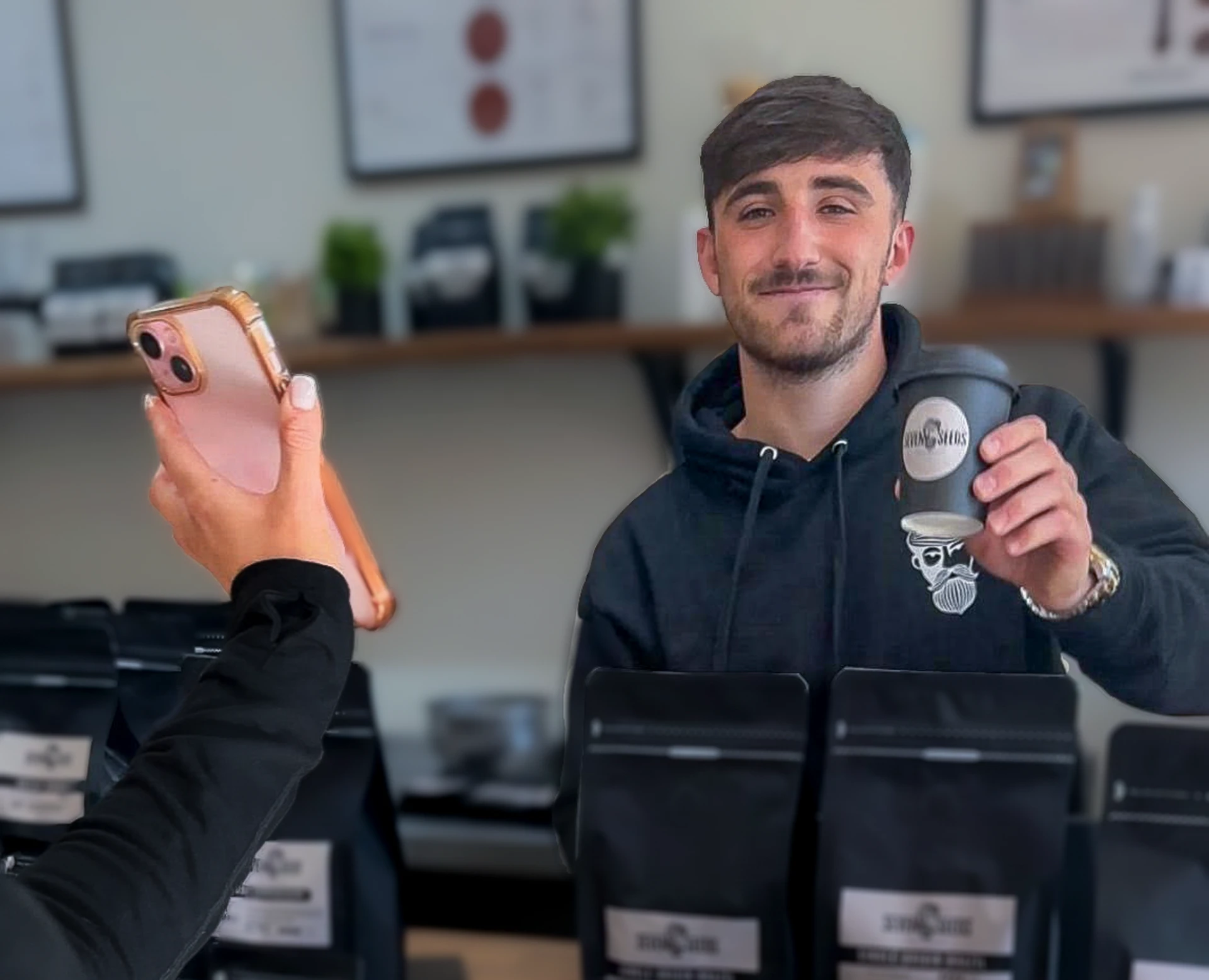 A customer photographing a barista holding a takeaway coffee at an independent coffee shop